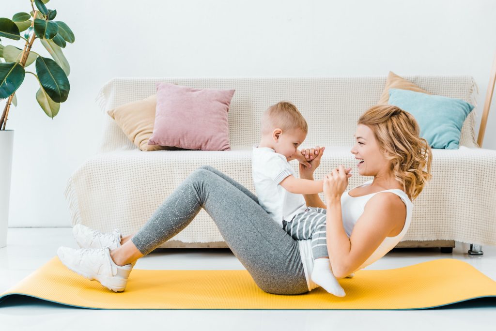 woman holding toddler son and training on fitness mat in living room